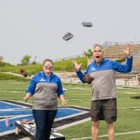 Scott Grissom and Lindsey Burns excitedly tossing cornhole bags into the air, while standing on the GVSU football field